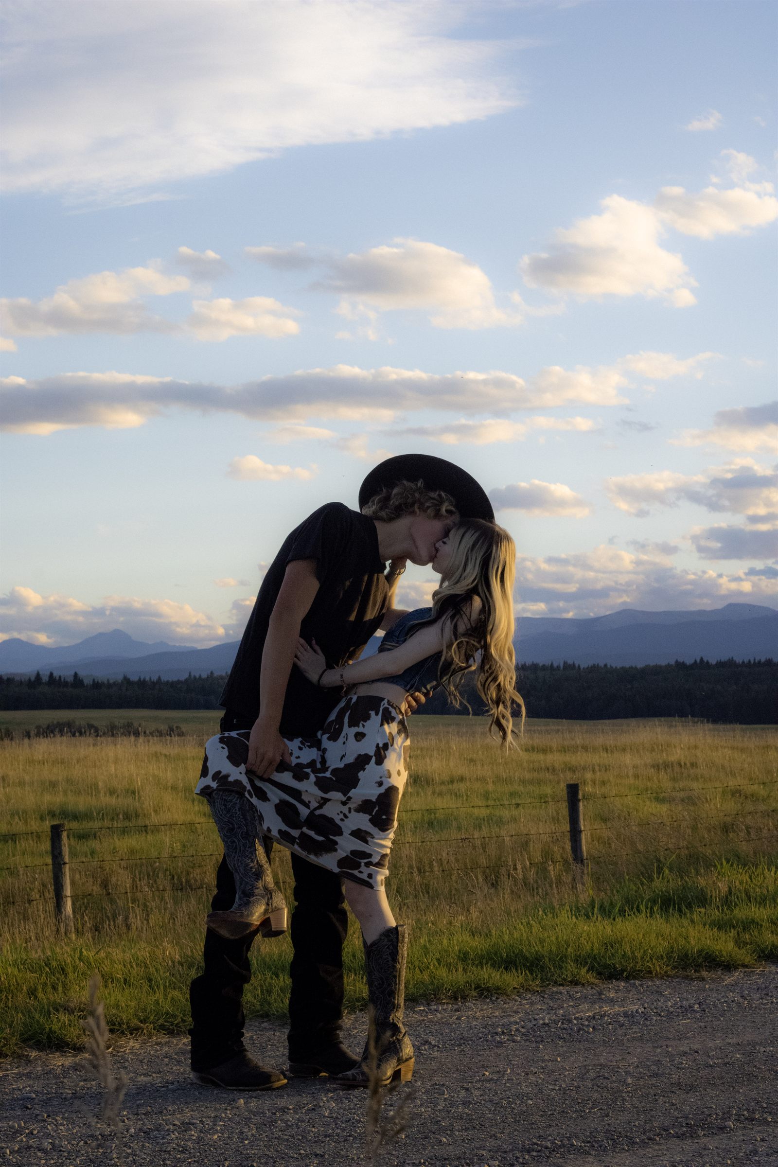 A couple in cowboy attire dipping into a kiss in a wide field.